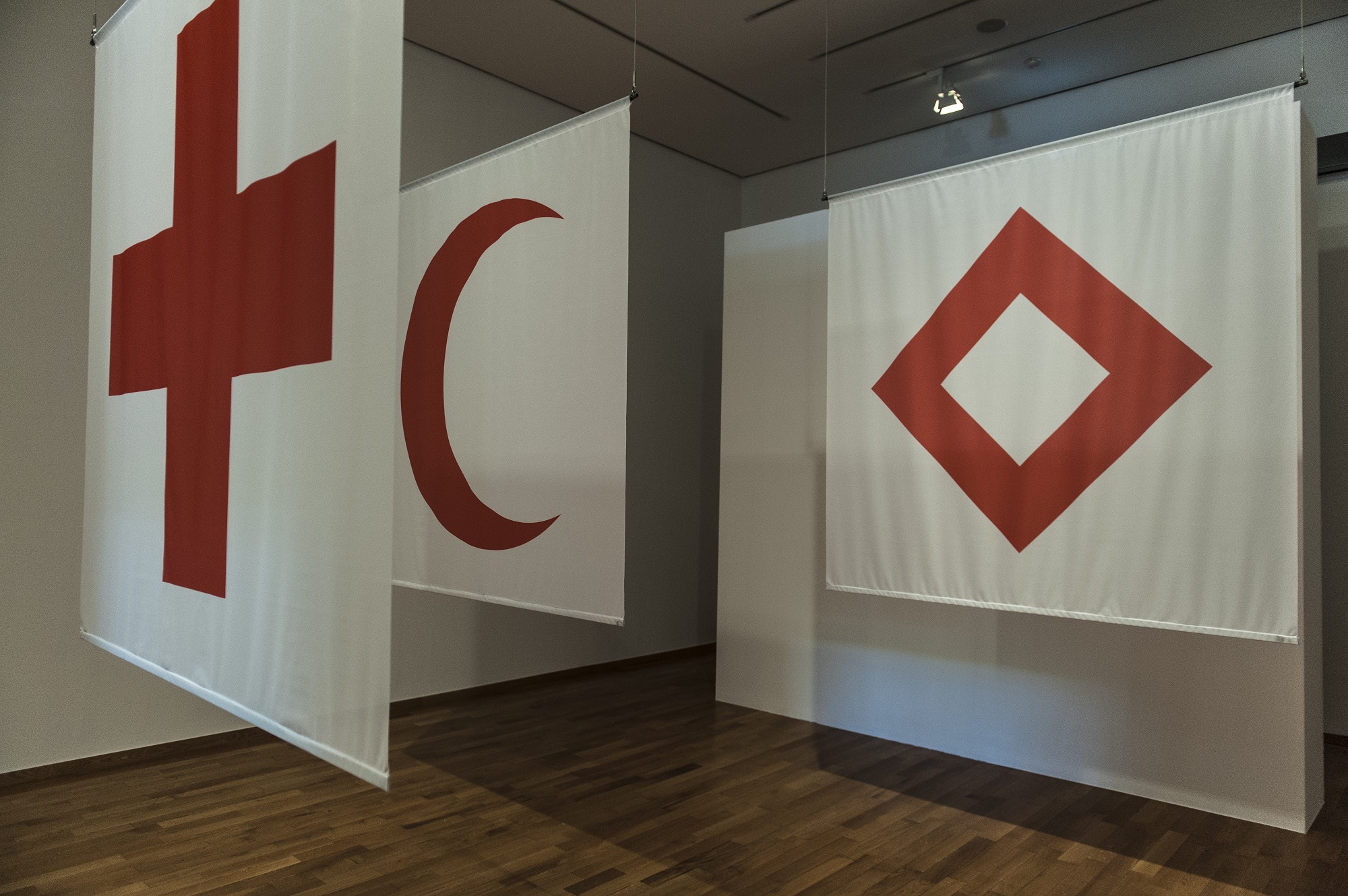 Inauguration of the exhibition "Humanizing War? 150 years of humanitarian history" at Musée Rath, in Geneva, in 2014, featuring the three emblems of the ICRC: the red cross, the red crescent, and the red crystal.  © ICRC Archives, Thierry Gassmann